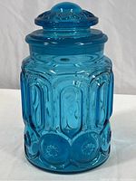 Front view of the blue glass apothecary jar showing embossed geometric patterns and circular floral motifs.