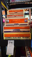 Stacked boxes of Lionel accessories including Coal Tipple Coal Pack, O Remote Control Track, Operating Lumberjacks, Mainline Auto Crossing Gates, and 072 Remote Switch Right Hand in original packaging with labels visible.