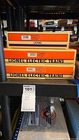 Three Lionel Electric Trains box cars series boxes stacked on black shelving displaying the side labels showing series and model numbers