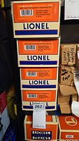 Stacked Lionel train car boxes showing model numbers and key features including illuminated interiors, die-cast metal trucks, and magnetic couplers.