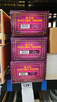Three stacked purple MTH Electric Trains boxes with product labels showing Heinz Reefer and Amtrak Mail Box car model numbers.