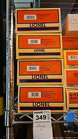 Four orange Lionel boxes stacked vertically showing model train car types and numbers on top labels.