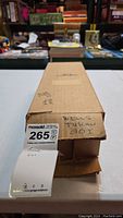 Photo of the box labeled 'WELLS TUSCAN GG1' with MaxSold lot tag number 265 attached