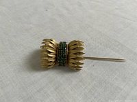 Oblique view of stick pin showing textured leaf fans and emerald-set central band