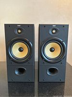 Front view of both speakers without grills showing woofers, tweeters, ports