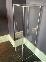 Front view of transparent square acrylic pedestal against wall