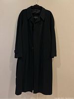 Full front view of black cashmere coat hanging against wall