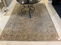 Full view of Persian-style rug laid on marble floor with iron coffee table showing overall pattern and size.