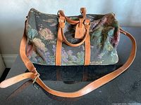 Full front view of floral tapestry overnight bag with top handles and shoulder strap laid out
