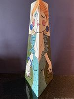 Front view of tall triangular vase showing the colorful female figure with orange hair, blue earrings, and blue-green dress on all three sides.
