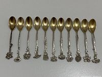 All 11 spoons arranged in a row showing gold-plated bowls and floral silver handles