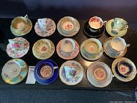 Full display of all fifteen vintage teacup and saucer pairs on black counter