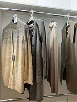 Four neutral-tone knit garments hanging on a clothing rack: ombré cardigan, gray cardigan, beige turtleneck, tan vest.