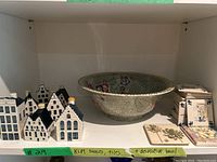 Shelf containing KLM blue and white ceramic houses, a large decorative bowl with floral textures, and ceramic tiles.