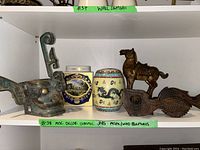 Shelf display with all items: metal animal head, two ceramic vessels, horse sculpture, and wooden carvings.