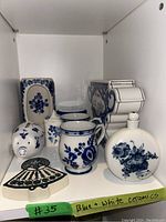 Blue and white ceramic vases, mugs, pig container, plate, and decorative item holder arranged on a white shelf.