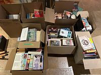 Wide shot of six boxes filled with assorted books showing stacked titles and varied subject matter