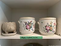 Front view of two large floral ceramic pots with gold rim and one beige hedgehog shaped pot.