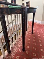 Side view showing tapered leg with gold decorative motifs and part of the table top.