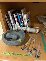 Photo showing assorted cookbooks, gray stone mortar and pestle, and white immersion blender corded appliance