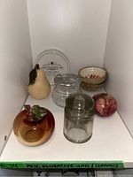 Shelf with assorted decorative glass and ceramic items including fruit-shaped pieces, glass jars, bowls, and plates