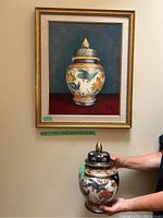 Photo showing the framed painting and the urn held below it to compare size and design