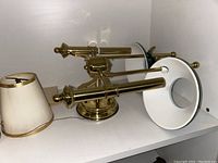 Photo of gold-colored wall sconce with white conical shade and two table lamp shades placed on a shelf.
