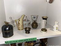 Overview showing all ceramic and metal vessels and decorative items on white shelf, including pitcher, vases, figurines, and containers.