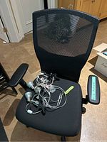 Black ergonomic office chair with mesh back and fabric seat, armrest with measurement label, and several clip-on spotlights placed on the seat.