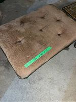 Large brown upholstered tufted rectangular ottoman with wooden legs, visible wear and staining on fabric.