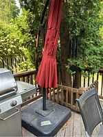 Assembled cantilever umbrella on deck near grill showing base, stand, and closed red canopy