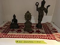 Three metal sculptures on a red and cream woven wool mat with fringe, items labeled #31 Sculptures + Mat