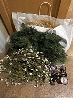Lot contents showing artificial green pine and white floral wreaths, natural wheat wreaths, metal bells with ribbons, and a candle holder.
