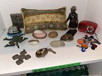 Overview of all items on white shelf including pillow, clock radio, figurine, assorted stones and shells, metal frog, metal cross, bell, and charms.
