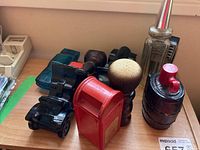 Seven vintage cologne bottles displayed on wooden surface including figurines shaped like cars, mailbox, barrel, pipe, goblet/brush, and ribbed glass bottle with metal dispenser.