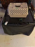 Plastic pet carrier placed on black surface, showing ventilation holes and handle.