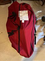 Red Christmas tree storage bag lying on a floor with zipper closure and carrying handles visible