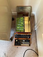 Photo of metal tin storage box open showing green Lego pieces organized inside, alongside wooden box containing cutlery set.