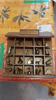 Wooden shadow box display shelf labeled 'ANTIQUES' containing 16 compartments with miniature metal figurines of teapots, pitchers, kettles, and other household items.