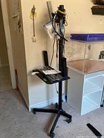 TV cart standing with cables hanging from the pole and instruction manual on the top shelf.