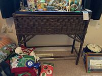Front view of the wicker plant stand showing its woven body, metal top, and surrounding items.