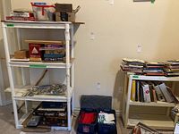 Four-tier large white plastic storage shelf with open shelves, showing wear and use, containing miscellaneous items not included in sale.