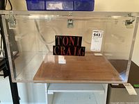 Front view of the clear plastic resin box with two metal latches and a visible label inside the box reading 'TONI CRAIG'.