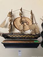 Front view of the fragile multi-masted ship replica model with fabric sails mounted on a decorated black wooden base.