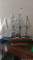 Wooden ship model with multiple sails and rigging on wooden base, partially wrapped in plastic