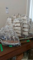 Three ship replica models placed on a wooden surface, wrapped in plastic for protection.