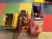 Photo showing the yellow bin with green toy soldiers, wooden play table, and Little Tykes shopping cart with black-haired doll inside