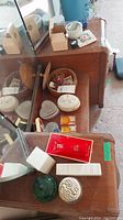 Wide view of wooden dresser surface with assorted trinket boxes, pins, sewing ephemera, and costume jewelry earrings in small dish.