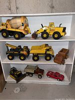 All seven Tonka toy vehicles displayed on white shelves showing wear and paint chipping