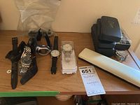 Lot of wrist watches including five watches with various bands displayed on a wooden surface alongside multiple watch cases and boxes and magnifiers.